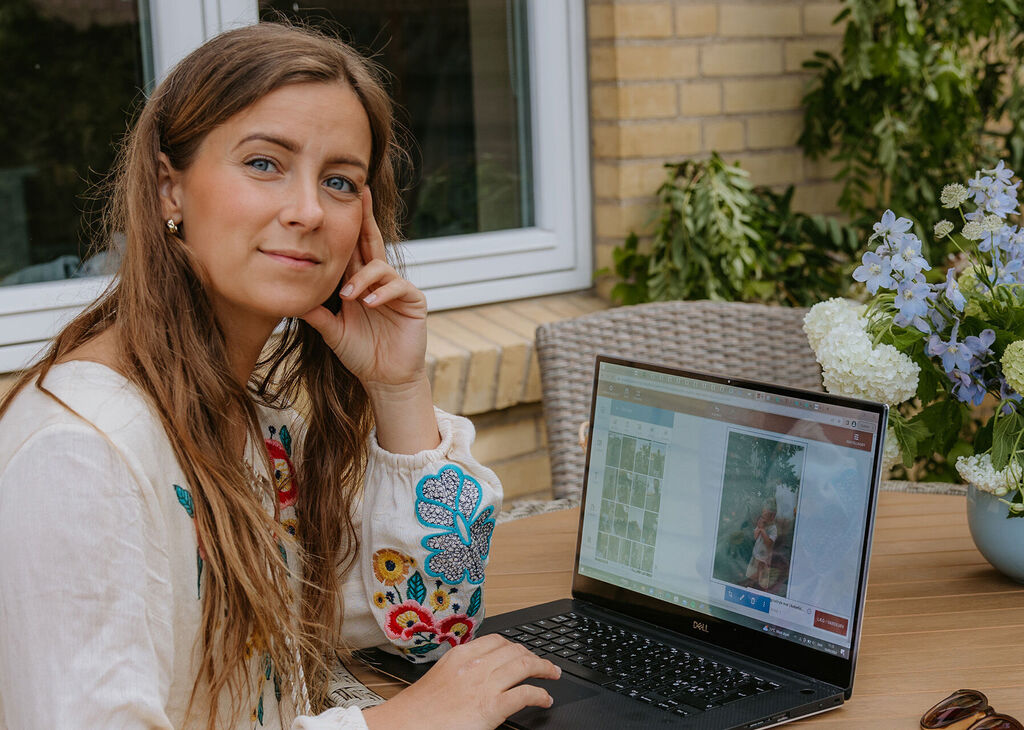 En person arbejder på en laptop udendørs med blomster og en afslappet atmosfære.